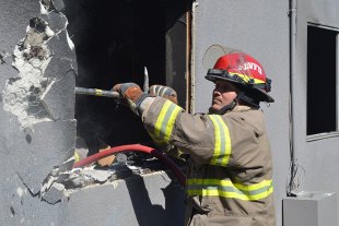 Lemoore firefighter Abi Shiyomura enlarges an opening to the apartment where the fire started.